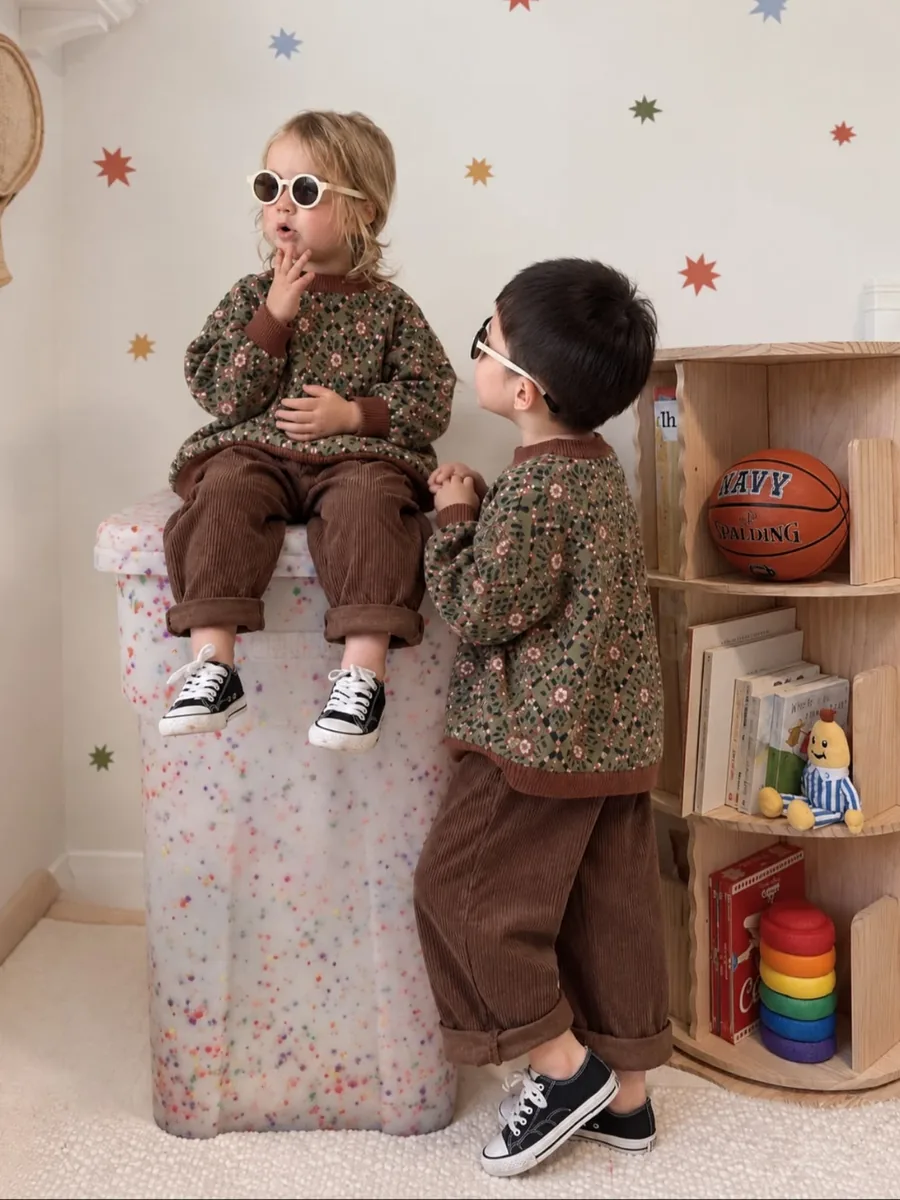 Two children wearing the sage green floral jacquard sweater with brown corduroy trousers