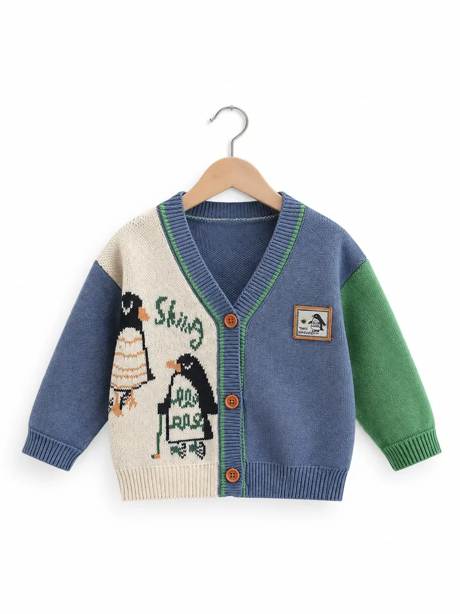 Kinkuu penguin knit cardigan: cream and blue front with two knitted penguins, green sleeve and orange buttons, on a hanger